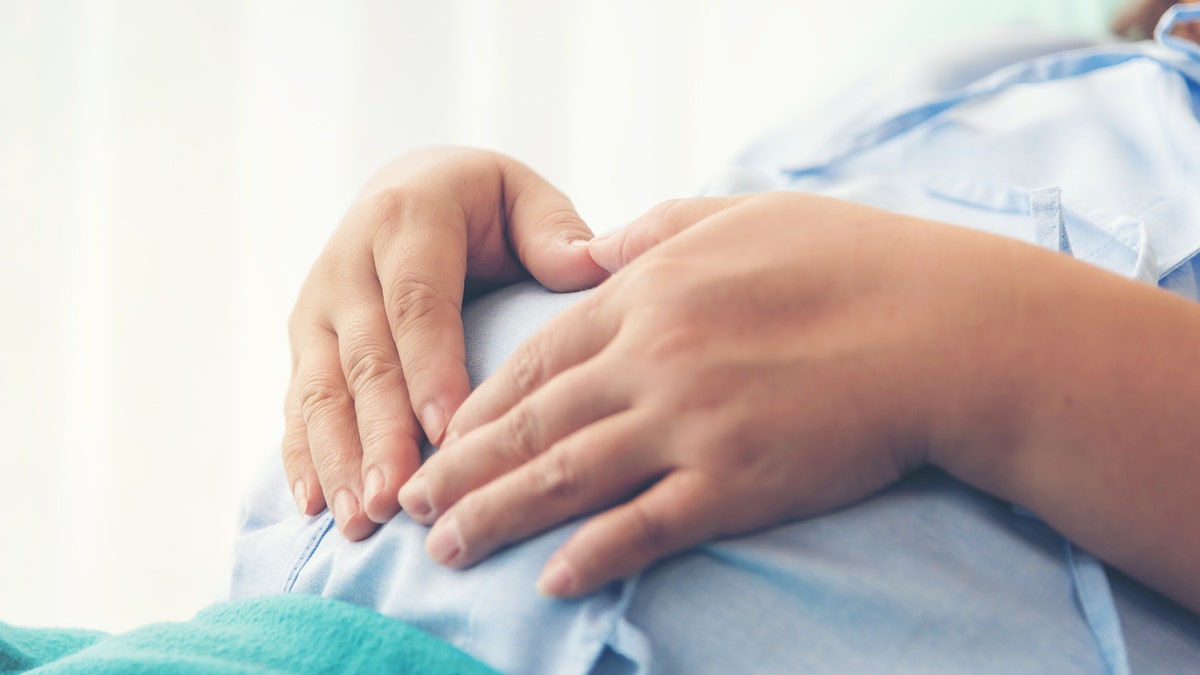 Pregnant woman holds belly from hospital bed