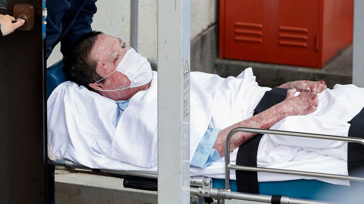 Shinji Aoba appeared on a stretcher as he was carried to Fushimi police station after being arrested in Kyoto, western Japan, Wednesday. (Suo Takekuma/Kyodo News via AP)