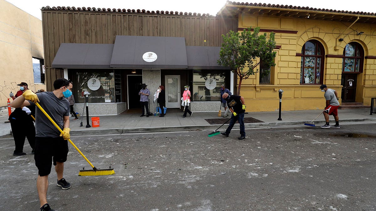 People helping clean up broken glass and debris after the riots over the death of George Floyd, Sunday in La Mesa, Calif. (AP Photo/Gregory Bull)