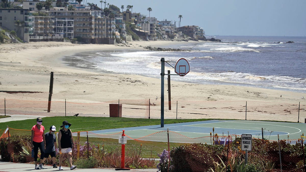 FILE - In this May 3, 2020 file photo people walk past a closed off beach, in Laguna Beach, Calif. Orange County's beachfront communities have submitted plans to reopen their beaches that adhere to California Gov. Gavin Newsom's stay-at-home order, the California Natural Resources Agency said in a statement. (AP Photo/Marcio Jose Sanchez,File)