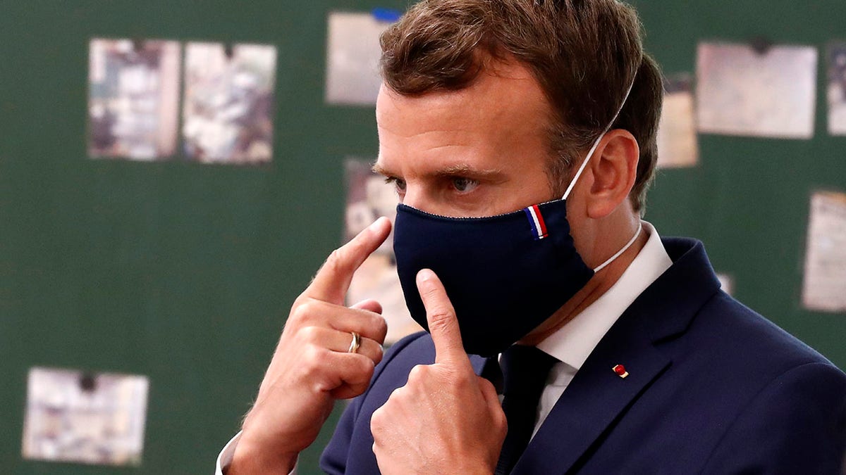 Macron wears a protective face mask with a blue-white-red colored ribbon as he speaks with schoolchildren during a class Tuesday while visiting the Pierre Ronsard elementary school in Poissy, outside Paris. (Ian Langsdon, Pool via AP)