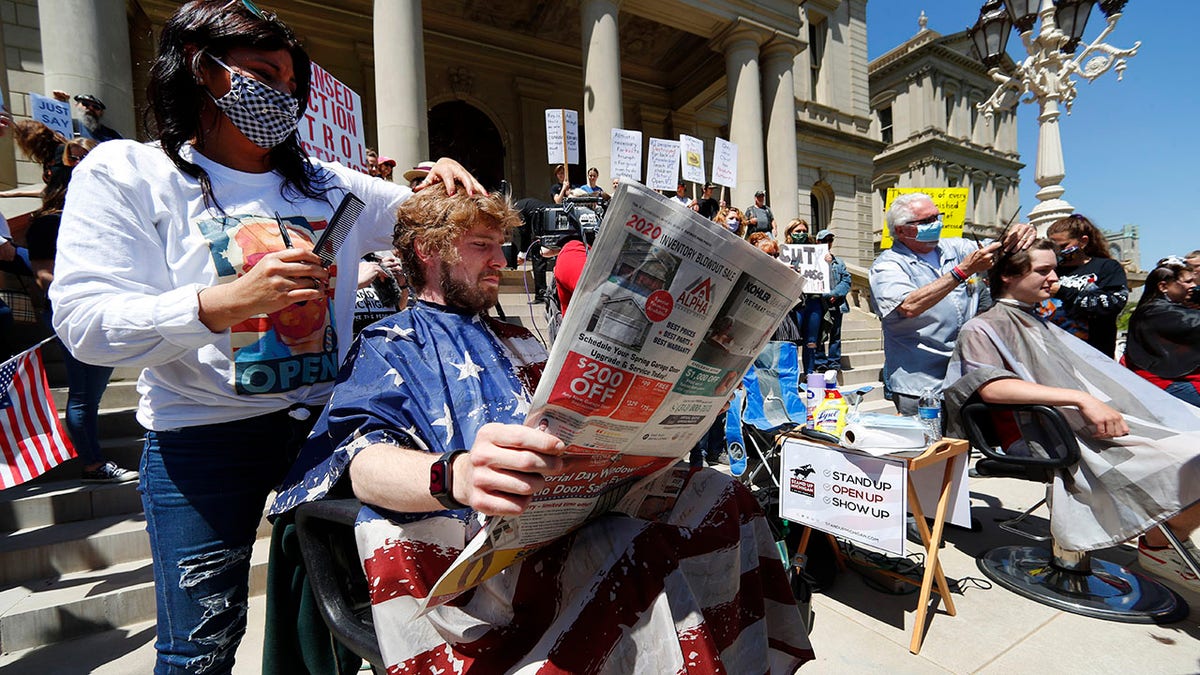 Jody Hebberd, left, gives a free haircut to Reid Scott, as he reads the paper on the steps of the State Capitol as Karl Manke, right, cuts the hair of Parker Shonts during a rally in Lansing, Mich., on Wednesday. (AP Photo/Paul Sancya)