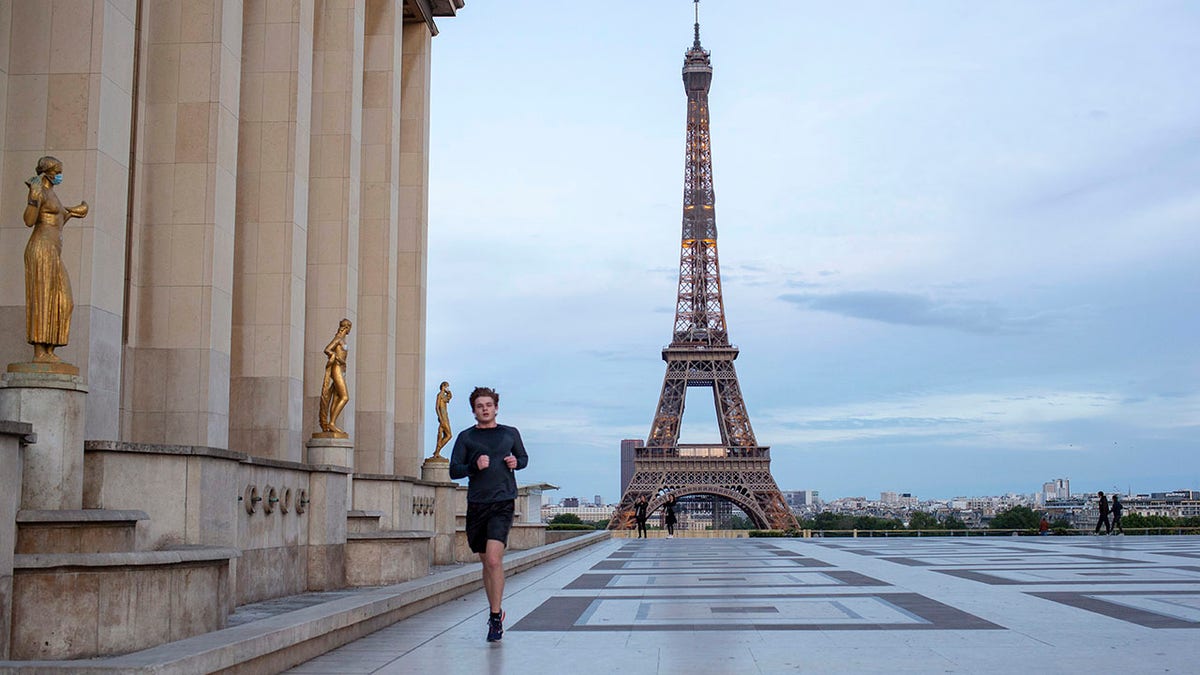 A man runs past some statues wearing face masks along the Trocadero square close to the Eiffel Tower during the coronavirus pandemic on Saturday. (AP Photo/Rafael Yahgobzadeh)