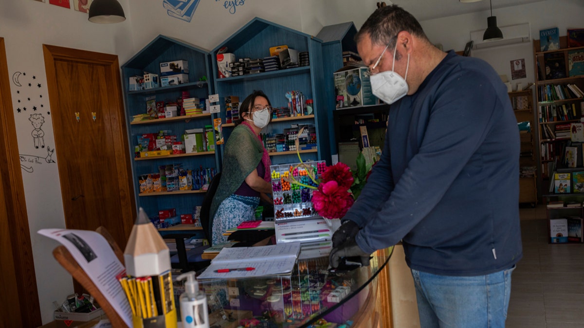 A stationary shop owner attends a customer in La Cabrera, outskirts of Madrid, Spain, Wednesday, May 6, 2020. The country enters the first stage of its 4-phase lockdown rollback helped by the lowest daily reports of coronavirus related deaths from coronavirus in 1.5 months.