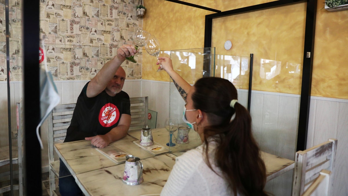 Manuel Gil, owner of company Llenatubar, simulates a toast in a coffee bar with worker Sheila on a table with methacrylate transparent screens built and installed by his company, following the outbreak of the coronavirus disease (COVID-19) in Leganes, Spain, April 24, 2020.