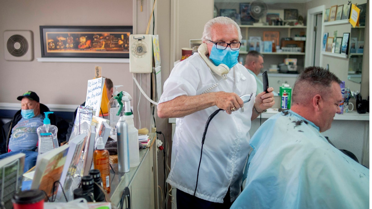 Karl Manke, 77, left, wears a mask while cutting hair, May 5, at Karl Manke's Barber and Beauty Shop in Owosso, Mich. Manke re-opened his doors on Monday in defiance of Gov. Gretchen Whitmer's executive order mandating salons, barbershops and other businesses to stay closed. He has already given nearly 100 haircuts, and fields more calls than that daily, all while continuing to cut hair. (Jake May/The Flint Journal via AP)
