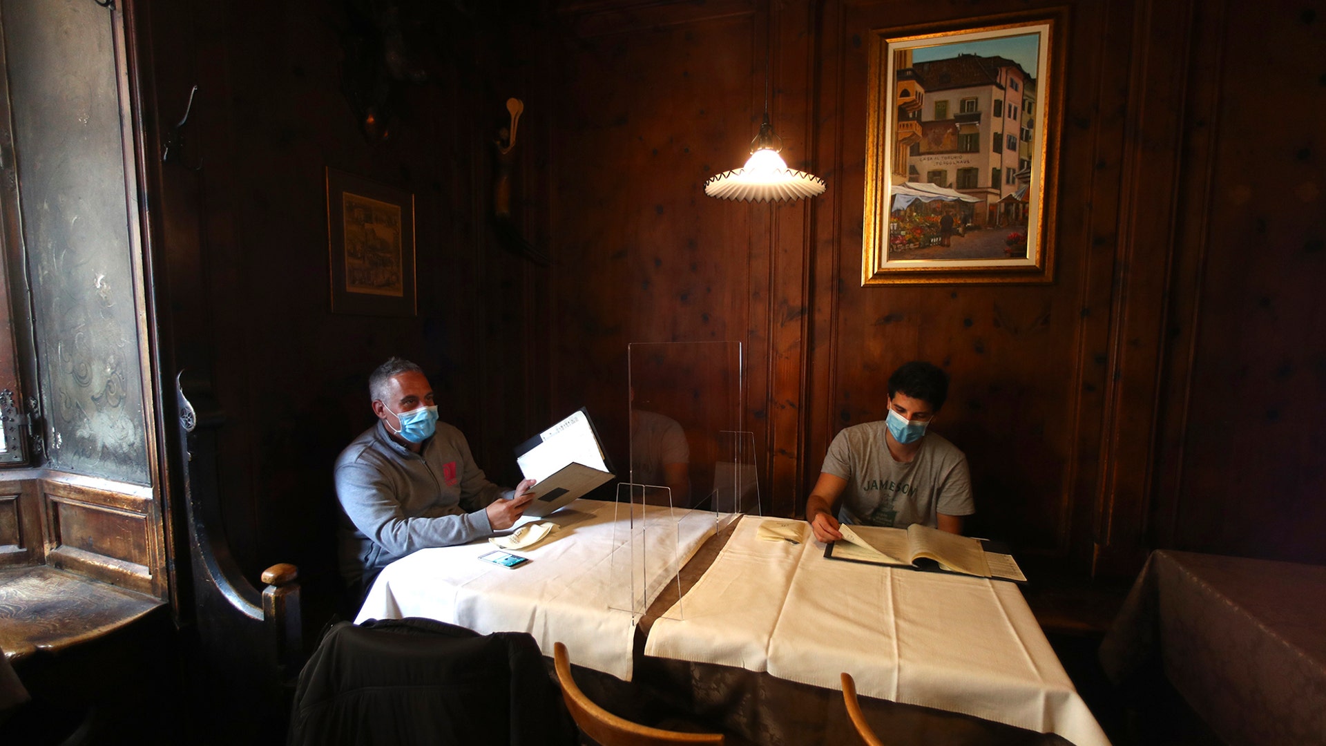 People wear masks to protect against the coronavirus as they sit next to a protective plastic window in a restaurant in Bozen, Italy, May 11, 2020. 