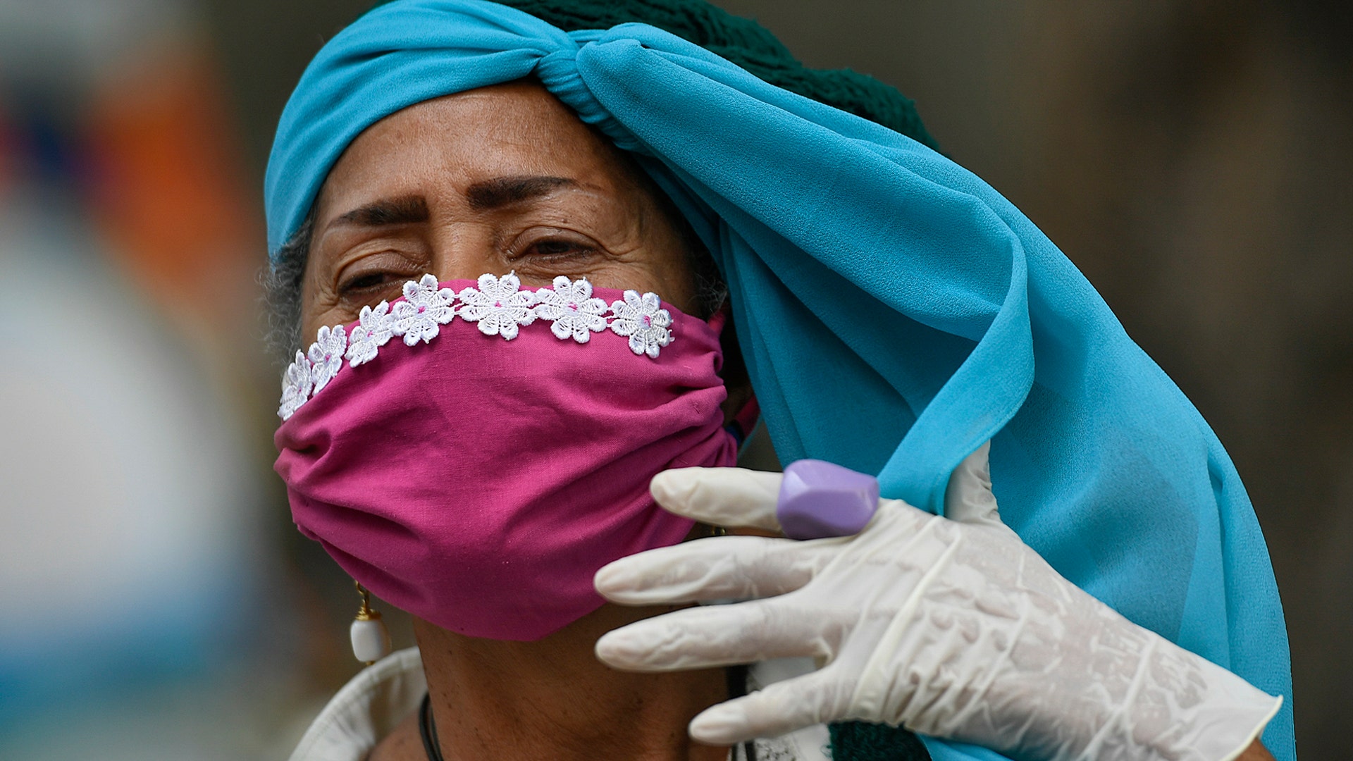 An elderly woman wearing a protective face mask and disposable gloves as a precaution against the spread of the coronavirus adjusts her headscarf as she takes a walk on the grounds of a nursing home in Caracas, Venezuela, May 2, 2020. 