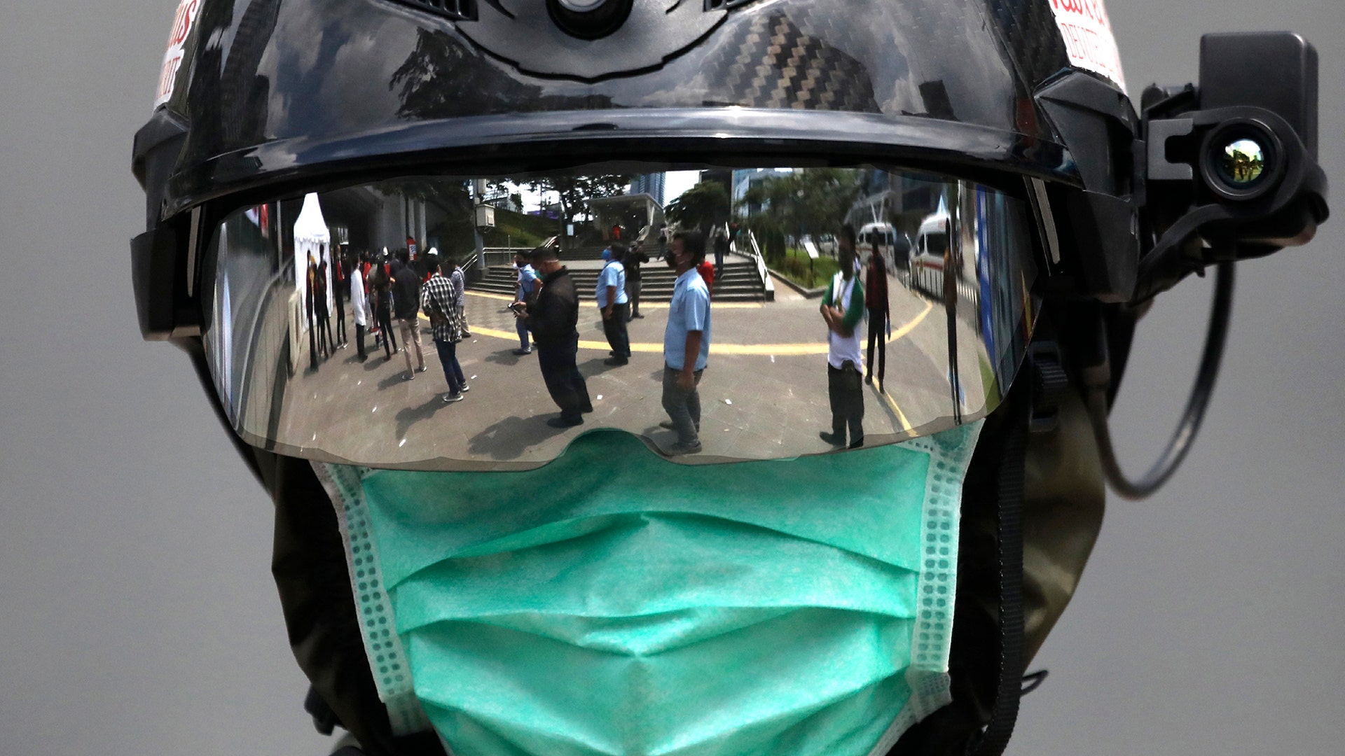 The reflection of people queuing to be tested for the coronavirus is seen on the visor of a medical official outside a mobile test site in Jakarta, Indonesia, May 6, 2020. 