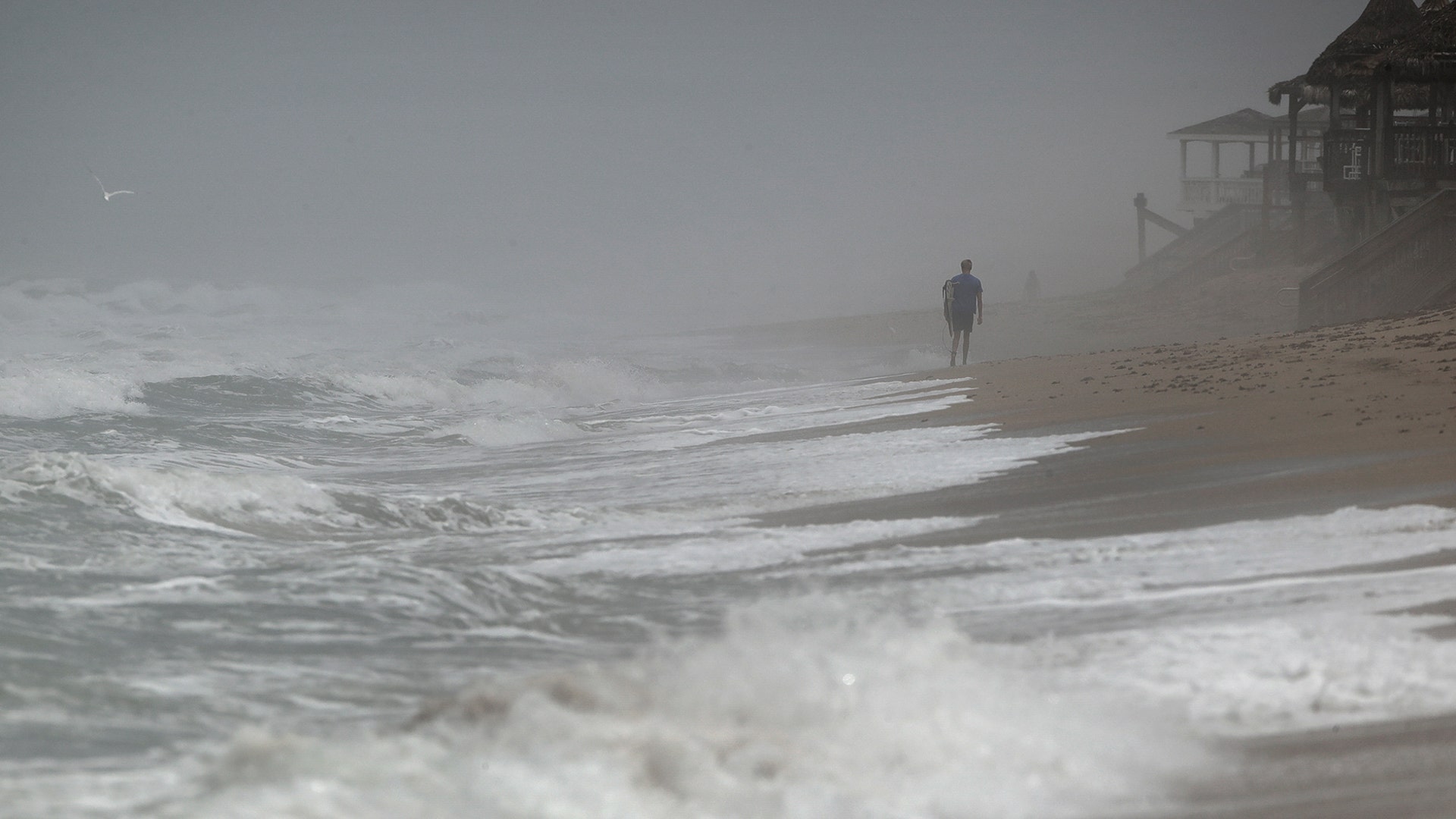 A surfer walks along an empty stretch of Bethune beach in New Smyrna Beach, Fla., May 26, 2020. 
