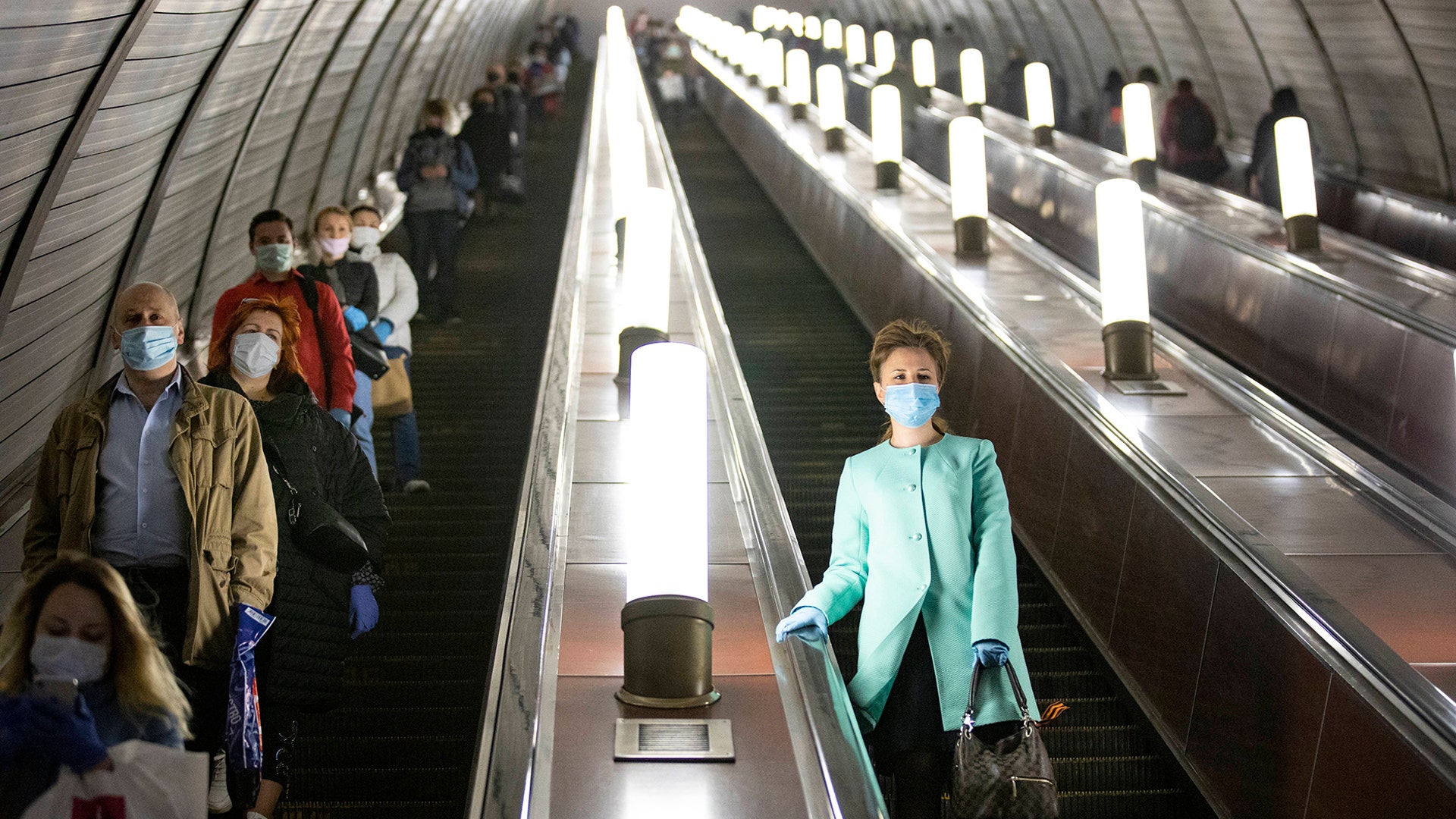 People wearing face masks and gloves to protect against coronavirus, observe social distancing guidelines as they go down the subway on the escalator in Moscow, May 12, 2020.