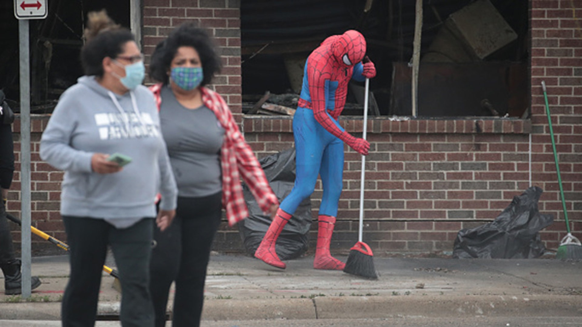 A person dressed as Spiderman sweeps the sidewalk as residents help to clean up following a night of rioting sparked by the death of George Floyd while in police custody on May 29, 2020 in Minneapolis.