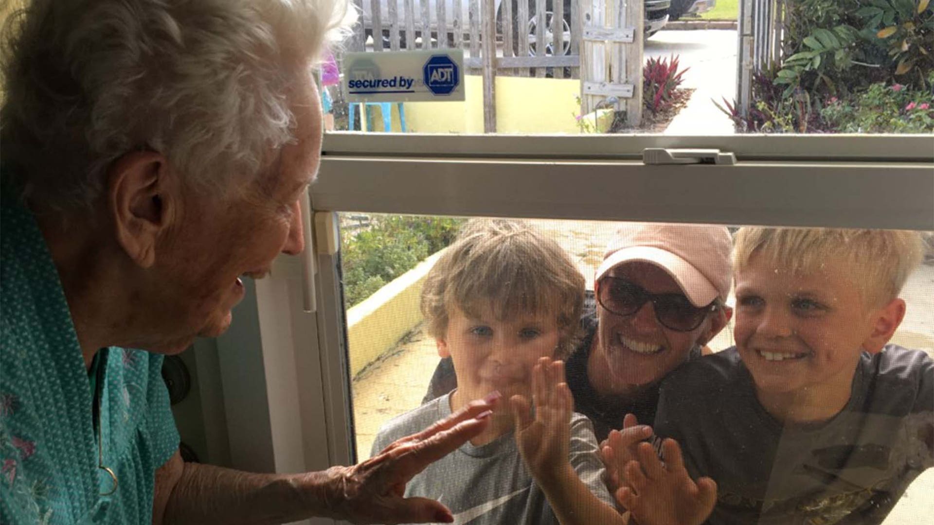 Virginia Smith, 95-year-old mother of four, 11 grandchildren and 17 great grandchildren, waves to two of her great grandchildren with their mother (l to r: Graham, Brinley, and Andrew) through the window of her daughter’s home in Jensen Beach FL. She would much rather be giving them a hug and a kiss than waving through the window but is doing her part and remaining isolated from the community.