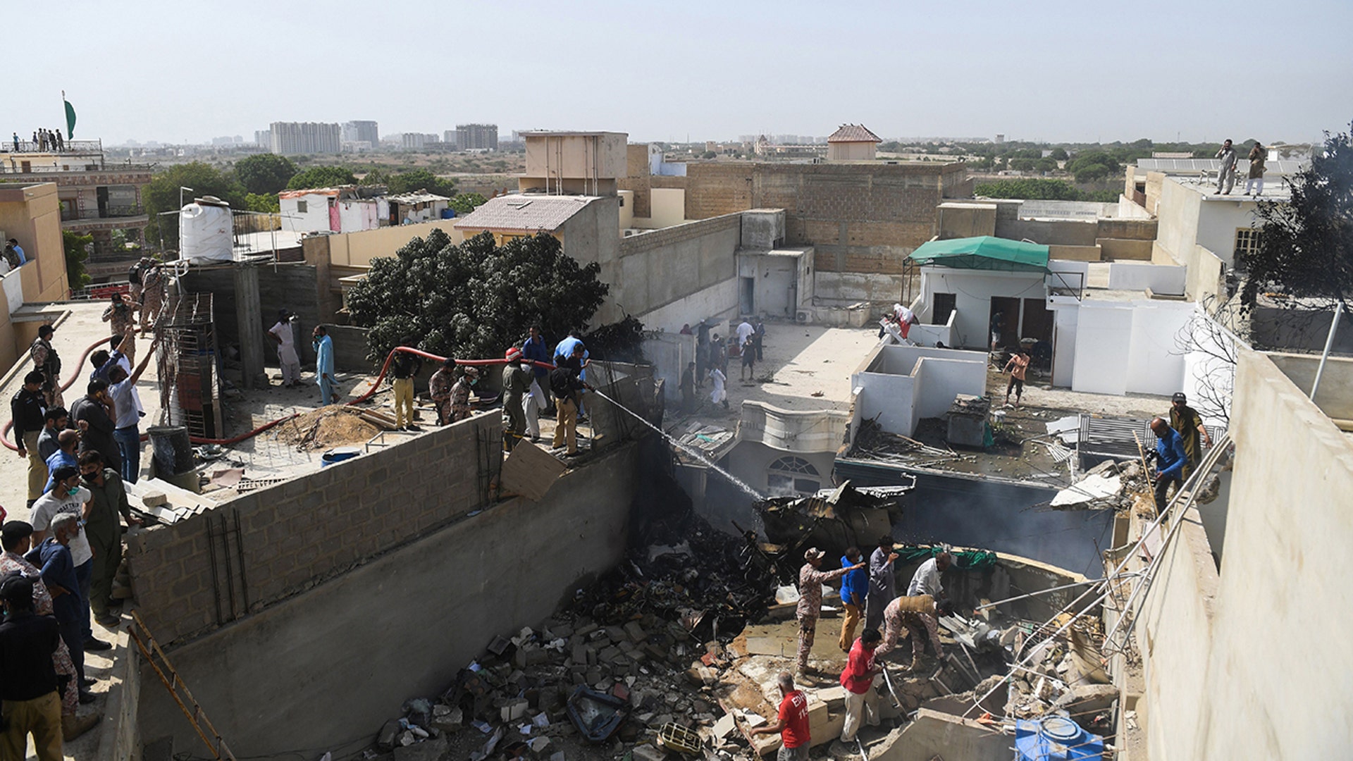 Rescue workers spray water on the part of a Pakistan International Airlines aircraft after it crashed at a residential area in Karachi on May 22, 2020. A Pakistan passenger plane with more than 100 people believed to be on board crashed in the southern city of Karachi on May 22, the country's aviation authority said. (Photo by Asif HASSAN / AFP)