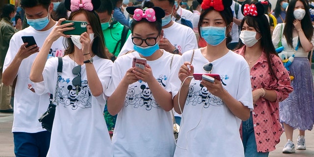 Visitors, wearing face masks, enter the Disneyland theme park in Shanghai as it reopened, Monday, May 11, 2020. Visits will be limited initially and must be booked in advance, and the company said it will increase cleaning and require social distancing in lines for the various attractions.(AP Photo/Sam McNeil)