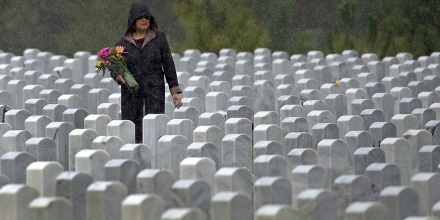 Bir kadın, Anma Günü için Cape Canaveral Ulusal Mezarlığı'nı ziyaret ederken yağmurda mezar arıyor