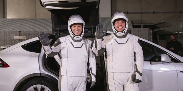 In this Friday, Jan. 17, 2020 photo made available by NASA, astronauts Doug Hurley, left, and Robert Behnken pose in front of a Tesla Model X car during a SpaceX launch dress rehearsal at Kennedy Space Center in Cape Canaveral, Fla. The NASA astronauts rode to the pad in the electric vehicle made by Elon Musk's company.