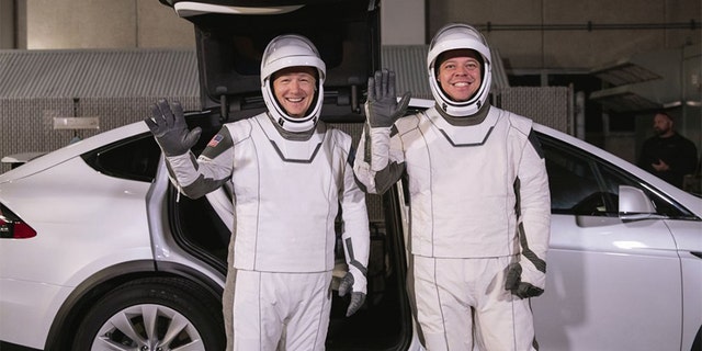 In this Friday, Jan. 17, 2020 photo made available by NASA, astronauts Doug Hurley, left, and Robert Behnken pose in front of a Tesla Model X car during a SpaceX launch dress rehearsal at Kennedy Space Center in Cape Canaveral, Fla. The NASA astronauts rode to the pad in the electric vehicle made by Elon Musk's company.