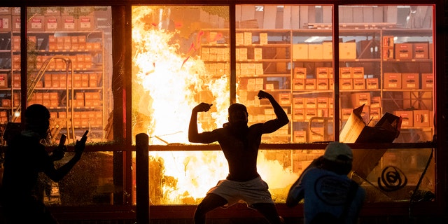 A man poses for photos in front of a fire at an AutoZone store, while protesters hold a rally for George Floyd in Minneapolis on Wednesday, May 27, 2020. Violent protests over the death of the black man in police custody broke out in Minneapolis for a second straight night Wednesday, with protesters in a standoff with officers outside a police precinct and looting of nearby stores. (Carlos Gonzalez/Star Tribune via AP)