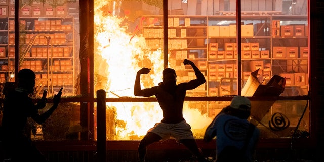 A man poses for photos in front of a fire at an AutoZone store, while protesters hold a rally for George Floyd in Minneapolis on Wednesday. (Carlos Gonzalez/Star Tribune via AP)