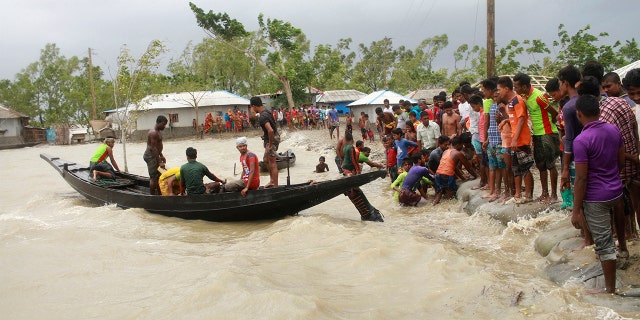 In this Wednesday, May 20, 2020 photo, a boat brings people to land, as locals check an embankment before Cyclone Amphan made landfall, in Shyamnagar, Shatkhira, Bangladesh.