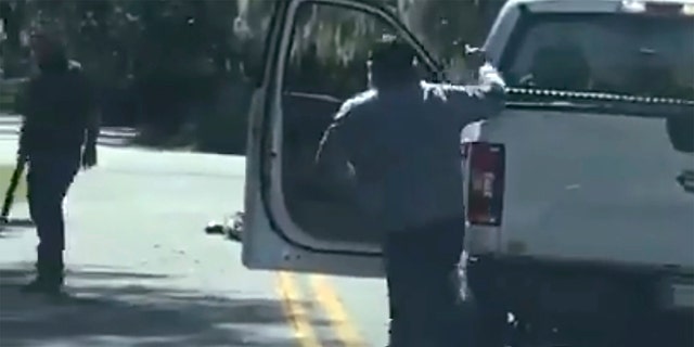 This image from video posted on Twitter Tuesday, May 5, 2020, shows Ahmaud Arbery lying on the road after being shot as Travis McMichael, left, holding a shotgun, and his father, Gregory McMichael, holding a handgun, approach him in a neighborhood outside Brunswick, Ga., on Feb. 23, 2020. (Twitter via AP)