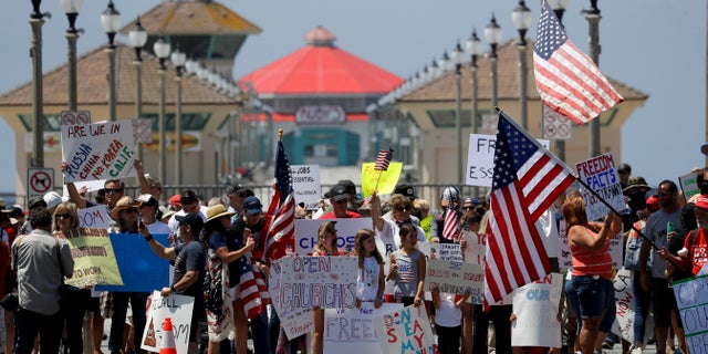 Protesters hold signs and wave flags during a demonstration at the pier Friday, May 1, 2020, in Huntington Beach, Calif., during the coronavirus outbreak. (Associated Press)