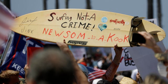 A protestor holds a hand painted sign on a surfboard during a demonstration at the pier, Friday, May 1, 2020, in Huntington Beach, Calif. (Associated Press)