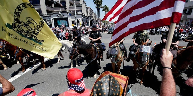 Law enforcement personnel on horseback keep protesters on the sidewalk during a demonstration at the pier Friday, May 1, 2020, in Huntington Beach, Calif., during the coronavirus outbreak. (Associated Press)