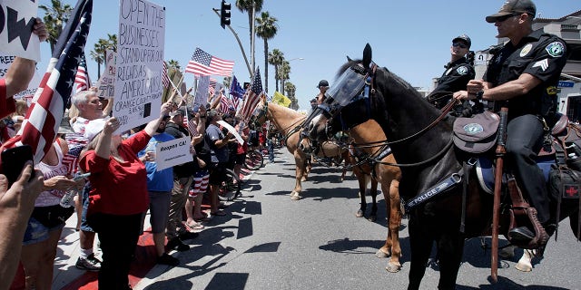 Law-enforcement personnel on horseback keep protesters on the sidewalk during a demonstration at the pier during the coronavirus pandemic Friday, May 1, 2020, in Huntington Beach, Calif. (Associated Press)