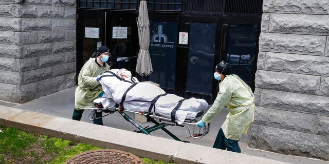 In this April 17 photo, a patient is wheeled out of the Cobble Hill Health Center by emergency medical workers in the Brooklyn borough of New York City.  (AP Photo/John Minchillo)