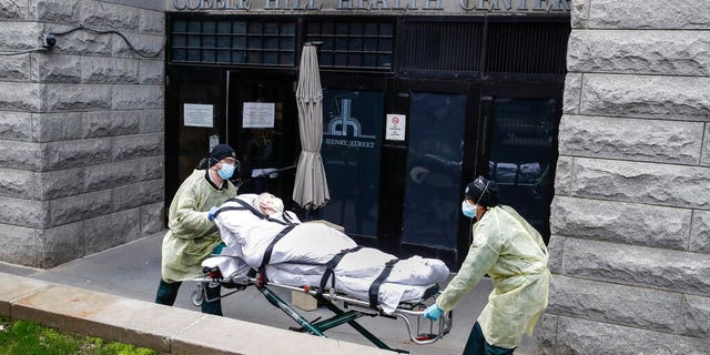 In this April 17 photo, a patient is wheeled out of the Cobble Hill Health Center by emergency medical workers in the Brooklyn borough of New York City.  (AP Photo/John Minchillo)