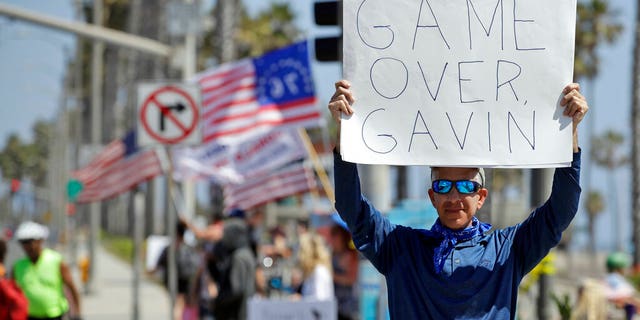 A protester holds a sign in front of the pier Sunday, May 3, 2020, in Huntington Beach, Calif. (Associated Press)