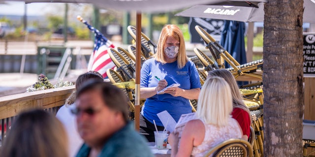 Jennifer Inman, wearing a mask, serves a table of diners at Dead Dog Saloon in Murrells Inlet, S.C. Rules for outdoor dining in South Carolina amid the coronavirus were relaxed on Monday. May 4, 2020. (Jason Lee/The Sun News via AP)