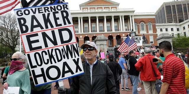 Demonstrators display flags and placards during a protest Monday in front of the Statehouse, in Boston. Protesters gathered in front of the Statehouse Monday to protest restrictions on movement and businesses prompted by the COVID-19 outbreak. (AP Photo/Steven Senne)