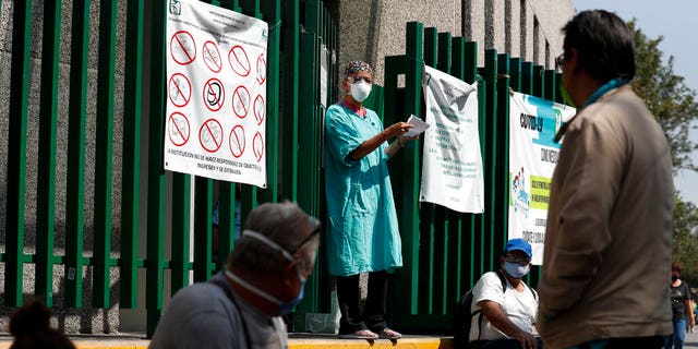 A hospital worker calls out a name from the gate, as relatives of hospitalized patients wait outside in hopes of receiving news of their loved ones, at a public hospital in the Iztapalapa district of Mexico City, Tuesday, May 5, 2020. 
