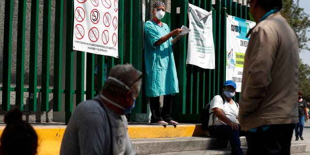 A hospital worker calls out a name from the gate, as relatives of hospitalized patients wait outside in hopes of receiving news of their loved ones, at a public hospital in the Iztapalapa district of Mexico City, Tuesday, May 5, 2020. Iztapalapa has the most confirmed cases of the new coronavirus within Mexico's densely populated capital, itself one of the hardest hit areas of the country with thousands of confirmed cases and around 500 deaths.(AP Photo/Rebecca Blackwell)