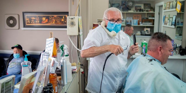 Karl Manke, 77, left, wears a mask while cutting hair on Tuesday at Karl Manke's Barber and Beauty Shop in Owosso, Mich. Manke re-opened his doors on Monday in defiance of Gov. Gretchen Whitmer's executive order mandating salons, barbershops and other businesses to stay closed. (Jake May/The Flint Journal via AP)