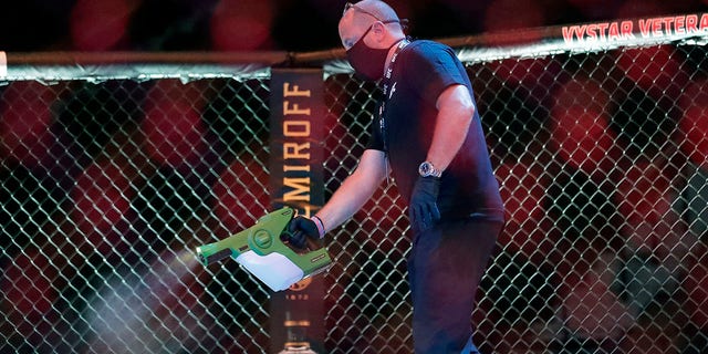 A worker sprays sanitizer in the octagon between bouts during a UFC 249 mixed martial arts competition, Saturday, May 9, 2020, in Jacksonville, Fla. (Associated Press)