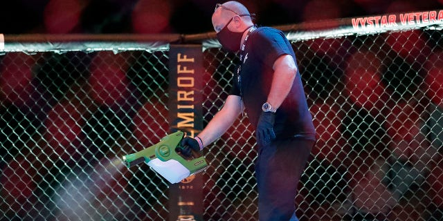A worker sprays sanitizer in the octagon between bouts during a UFC 249 mixed martial arts competition, Saturday, May 9, 2020, in Jacksonville, Fla. (Associated Press)