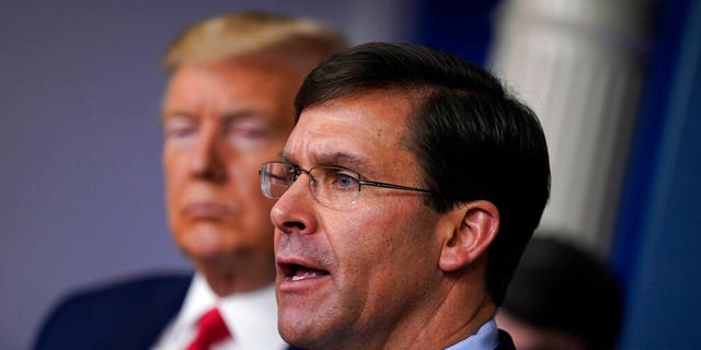 FILE - In this March 18, 2020, file photo, Defense Secretary Mark Esper speaks as President Donald Trump listens during press briefing with the coronavirus task force, at the White House in Washington. The government’s $3 trillion effort to rescue the economy from the coronavirus crisis is stirring worry at the Pentagon. Bulging federal deficits may force a reversal of years of big defense spending gains and threaten prized projects like the rebuilding of the nation’s arsenal of nuclear weapons. Esper says the sudden burst of emergency spending to prop up a stalled economy is bringing the Pentagon closer to a point where it will have to shed older weapons faster and tighten its belt. (AP Photo/Evan Vucci, File)