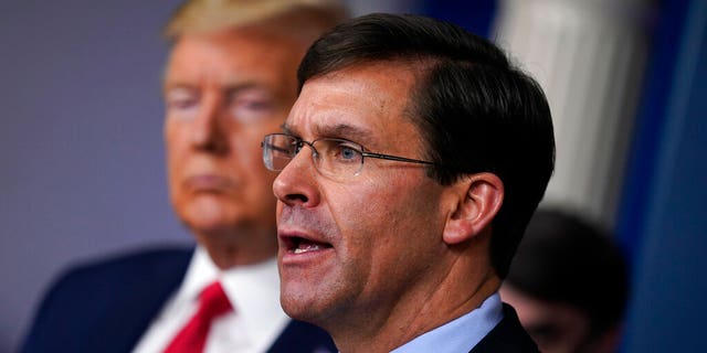 FILE - In this March 18, 2020, file photo, Defense Secretary Mark Esper speaks as President Donald Trump listens during press briefing with the coronavirus task force, at the White House in Washington. The government’s $3 trillion effort to rescue the economy from the coronavirus crisis is stirring worry at the Pentagon. Bulging federal deficits may force a reversal of years of big defense spending gains and threaten prized projects like the rebuilding of the nation’s arsenal of nuclear weapons. Esper says the sudden burst of emergency spending to prop up a stalled economy is bringing the Pentagon closer to a point where it will have to shed older weapons faster and tighten its belt. (AP Photo/Evan Vucci, File)