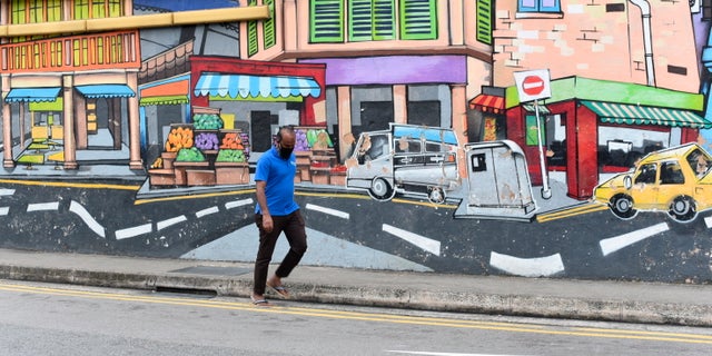 A man with a facemask walks past a wall mural in Singapore’s Little India district on Saturday, May 16, 2020. (AP Photo/YK Chan)