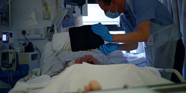 Chaplain David Anderson helps a patient communicate with his family that are unable to visit due to hospital visiting restrictions using the Zoom app on an iPad on Ward D1 at the Royal Blackburn Teaching Hospital, in Blackburn, England on May 14, amid the coronavirus pandemic. (Hannah McKay/Pool Photo via AP)