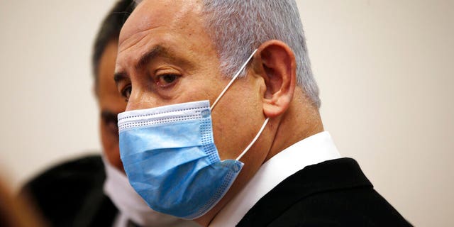 Israeli Prime Minister Benjamin Netanyahu, wearing a face mask in line with public health restrictions due to the coronavirus pandemic, standing inside the courtroom as his corruption trial started at the Jerusalem District Court.