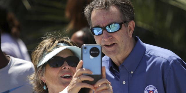 In this Saturday, May 23, 2020, photo, Gov. Ralph Northam and Tori Bloxom, of Onancock, Va., take a selfie as the governor visits the Oceanfront in Virginia Beach, Va., to see for himself how crowded the beach was. Northam has repeatedly urged Virginia residents to cover their faces in public during the COVID-19 pandemic, but the Democrat didn’t heed his own plea when he posed mask-less for photographs alongside residents during the weekend beach visit. A spokeswoman for the governor’s office said on Sunday that Northam should have brought a face mask with him during his visit on Saturday to the Virginia Beach Oceanfront. (Stephen M. Katz/The Virginian-Pilot via AP)