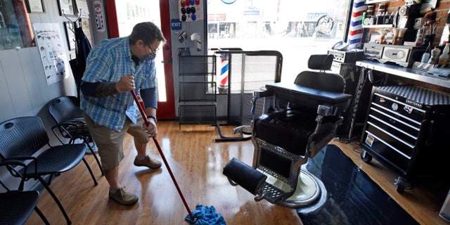 Mike Douglass, owner of the East J Barbershop, mops the floor of his shop on May 27 in Sacramento, Calif. Douglass said he will reopen in a few days so he has time to get his shop ready to adhere to the new guidelines that must be followed due to the coronavirus pandemic. (AP Photo/Rich Pedroncelli)