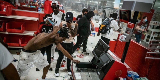 In this Wednesday, May 27, 2020 photo, a looter uses a claw hammer as he tries to break in to a cash register at a Target store in Minneapolis. Rioters ignited fires and looted stores all over the city, as peaceful protests turned increasingly violent in the aftermath of the death of George Floyd. (Richard Tsong-Taatarii/Star Tribune via AP)