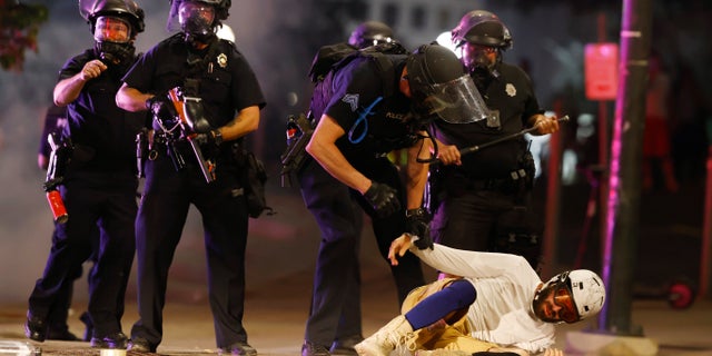 Denver Police Department officers clear a man who fell to the street after they used tear gas and rubber bullets to disperse a protest outside the State Capitol over the death of George Floyd, a handcuffed black man who died in police custody in Minneapolis, late Thursday, May 28, 2020, in Denver. (AP Photo/David Zalubowski)