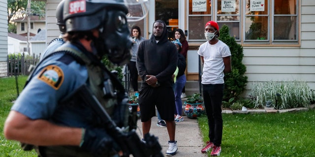 Protestors watch as police in riot gear walk down a residential street, Thursday, May 28, 2020, in St. Paul, Minn. Protests over the death of George Floyd, a black man who died in police custody Monday, broke out in Minneapolis for a third straight night. (AP Photo/John Minchillo)